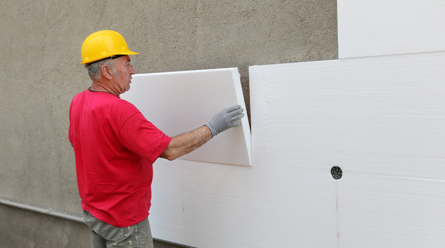Ouvriers spécialisés installant des panneaux d'isolation thermique par l'extérieur sur la façade d'un immeuble de bureaux